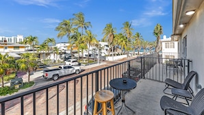 A balcony with wicker furniture, a view of the street, and palm trees. - Sun Beach Inn (Hollywood)