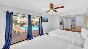 A hotel room with two beds, a ceiling fan, a view of a swimming pool, and a small kitchenette. - Sun Beach Inn (Hollywood)