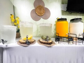 A table with three large beverage dispensers, a small sink, and a decorative wall piece.