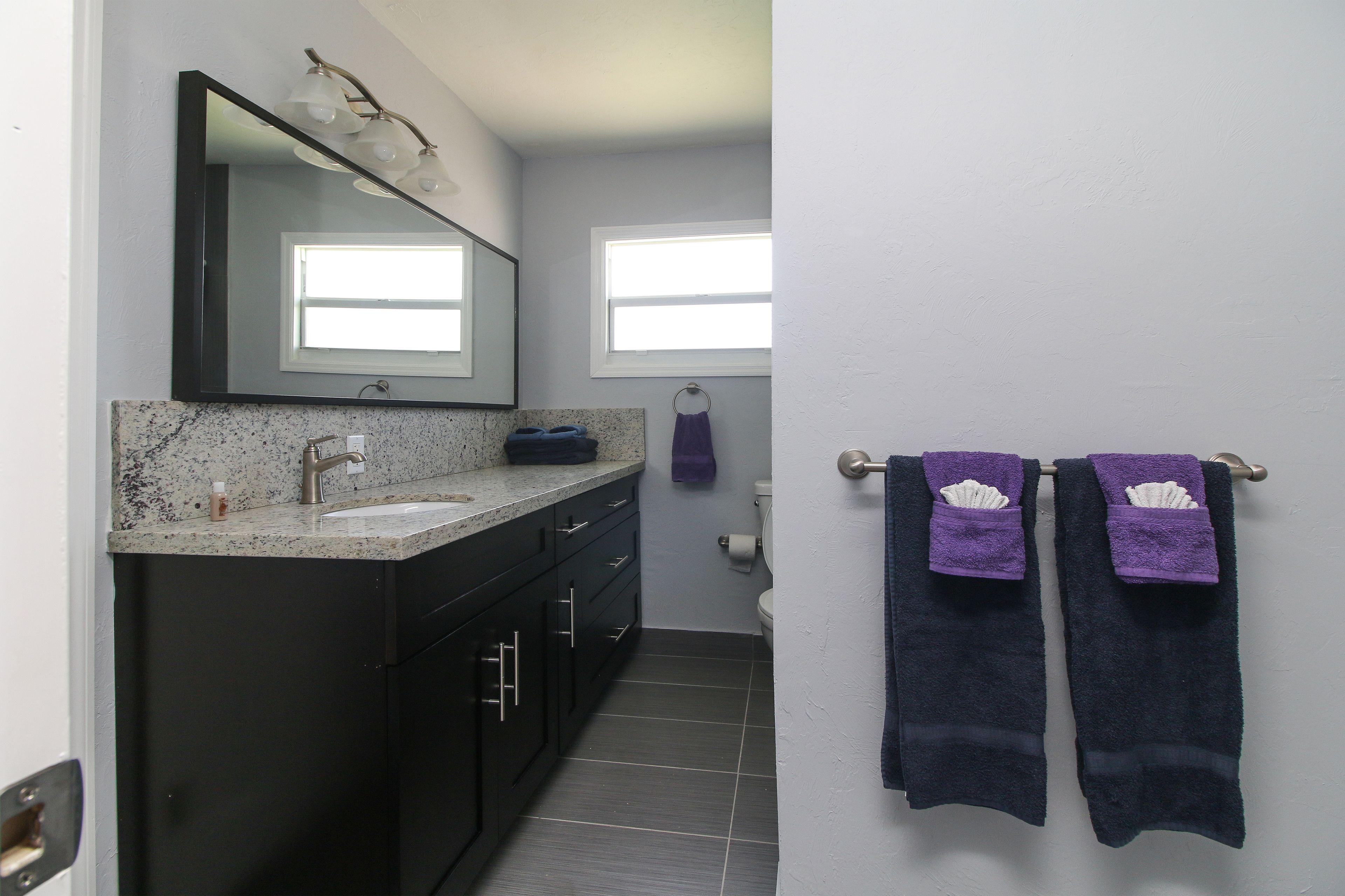 A bathroom with a dark vanity, a sink, and a mirror. There are two towels hanging on a rack.