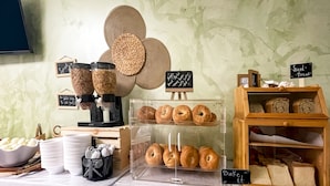 A bakery display with various baked goods, including bagels and bread, and a coffee machine. - Sun Beach Inn (Hollywood)