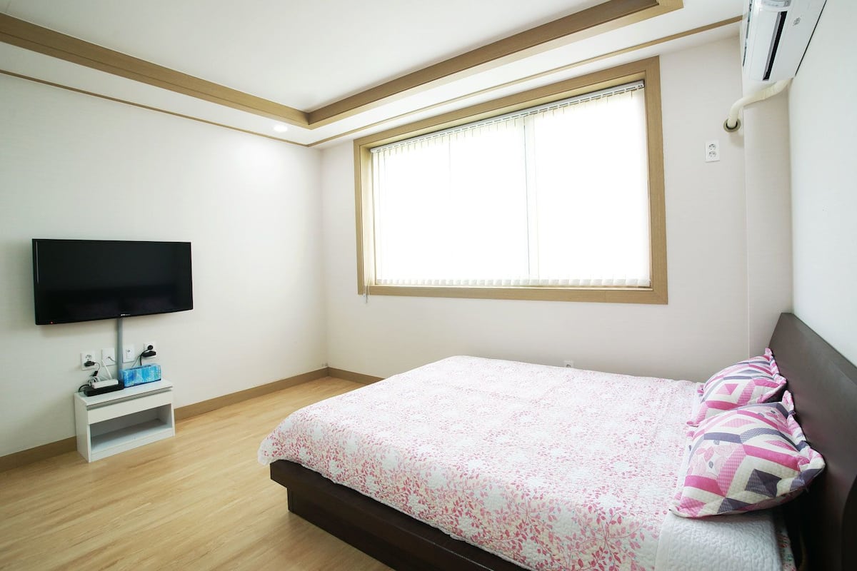 Un dormitorio con cama, televisión, ventana y aire acondicionado.