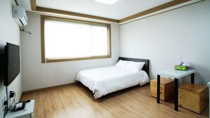 Une chambre à coucher avec un lit, un bureau, une télévision et une fenêtre.