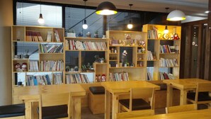 Une bibliothèque chaleureuse, avec des étagères en bois remplies de livres et d’objets décoratifs. On y trouve des tables et des bancs en bois pour s’asseoir.