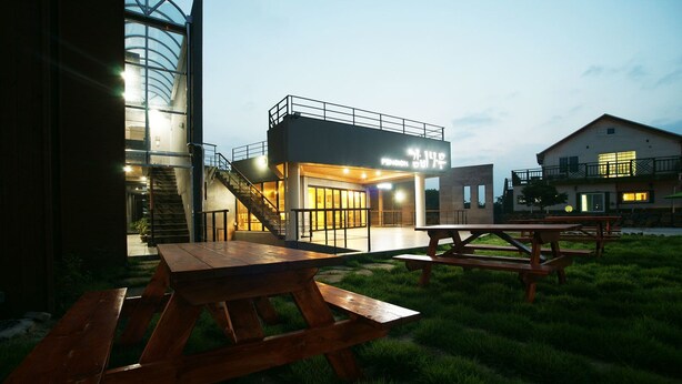 Un bâtiment moderne doté d’une façade en verre et d’un escalier menant à un niveau supérieur. On aperçoit des tables de pique-nique au premier plan.