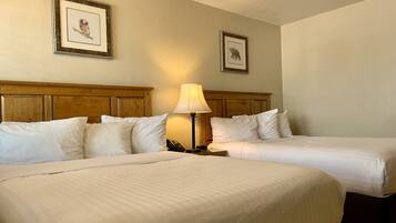 A hotel room with two beds, a wooden headboard, a bedside lamp, and framed pictures on the wall.