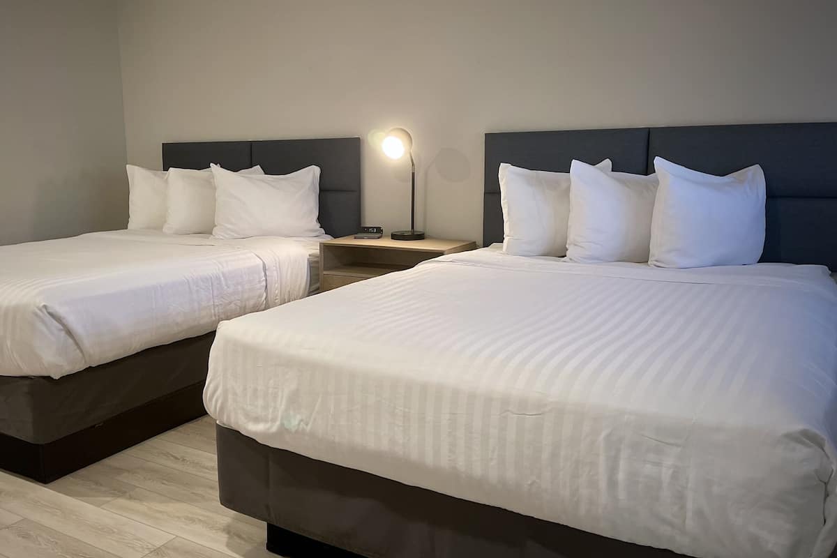 Deux lits simples avec des têtes de lit sombres et une literie blanche dans une chambre d’hôtel.