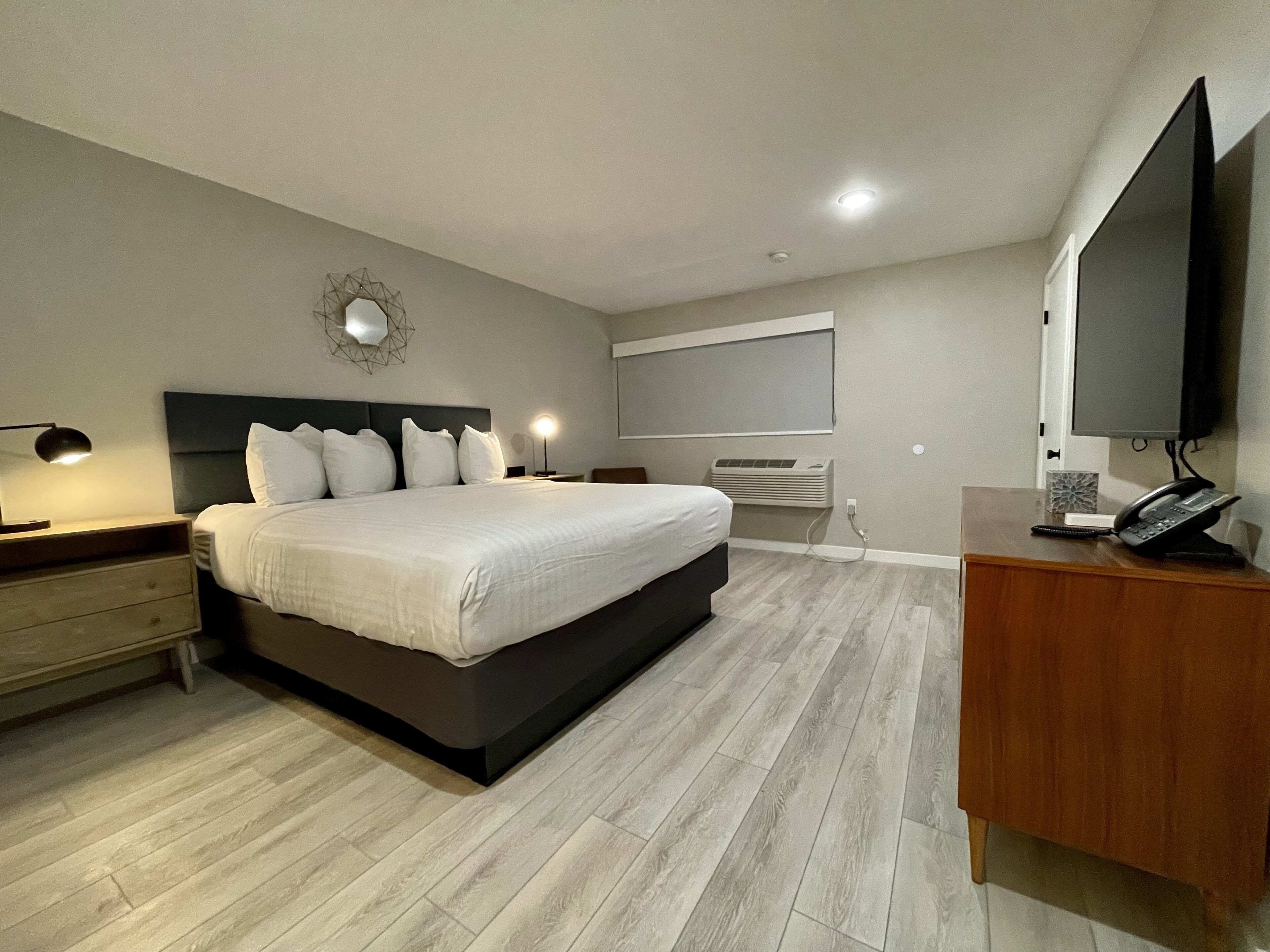 A modern bedroom with a large bed, bedside lamps, a flat-screen TV, a desk with a telephone, and a wall-mounted air conditioner.