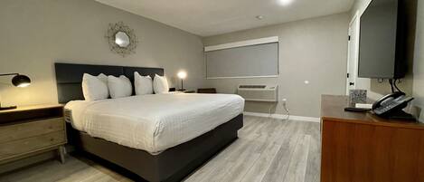 A modern bedroom with a large bed, bedside lamps, a flat-screen TV, a desk with a telephone, and a wall-mounted air conditioner.