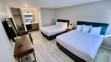 A hotel room with two single beds, a desk, a chair, a mirror, a small table, and a bathroom visible through an open door.