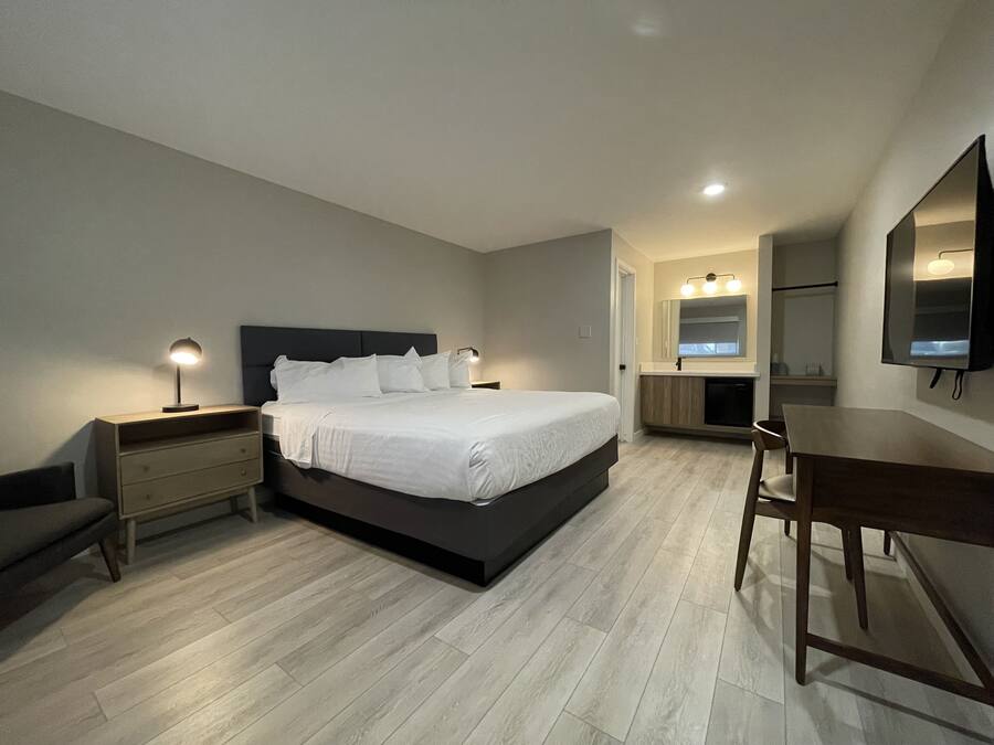 A modern bedroom with a large bed, bedside tables, a desk, and a mirror.