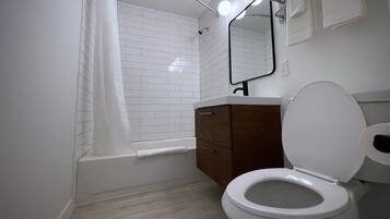 Une salle de bain avec des toilettes blanches, un meuble en bois et des murs recouverts de carreaux blancs.