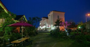 A courtyard with a dining area, outdoor seating, and a building with illuminated windows. - Lapaloma Pension (Jeju City)