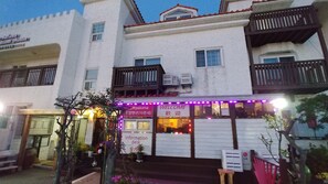 A building with a white facade, multiple windows, and balconies. There is a sign with 'Welcome' and 'Information Desk' visible. - Lapaloma Pension (Jeju City)