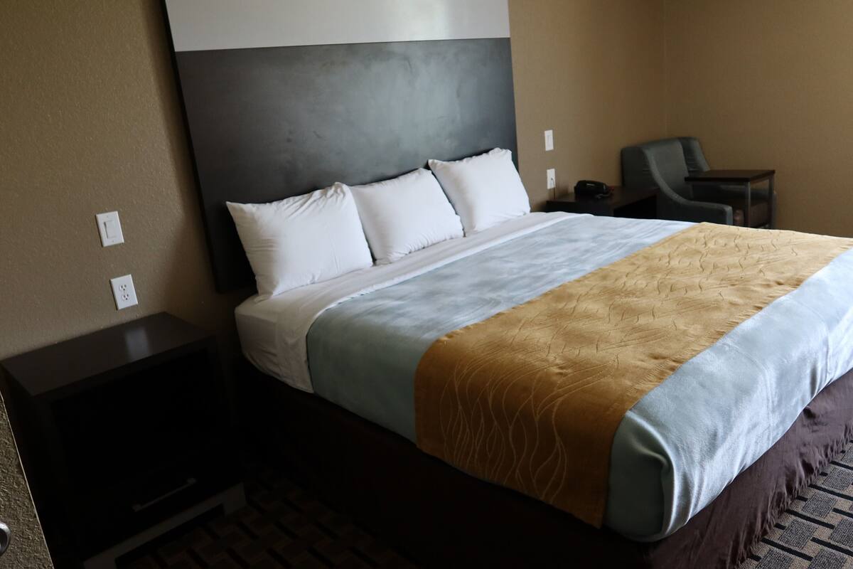 Ein Hotelzimmer mit einem großen Bett, einem Nachttisch, einem Sessel und einem Schreibtisch.