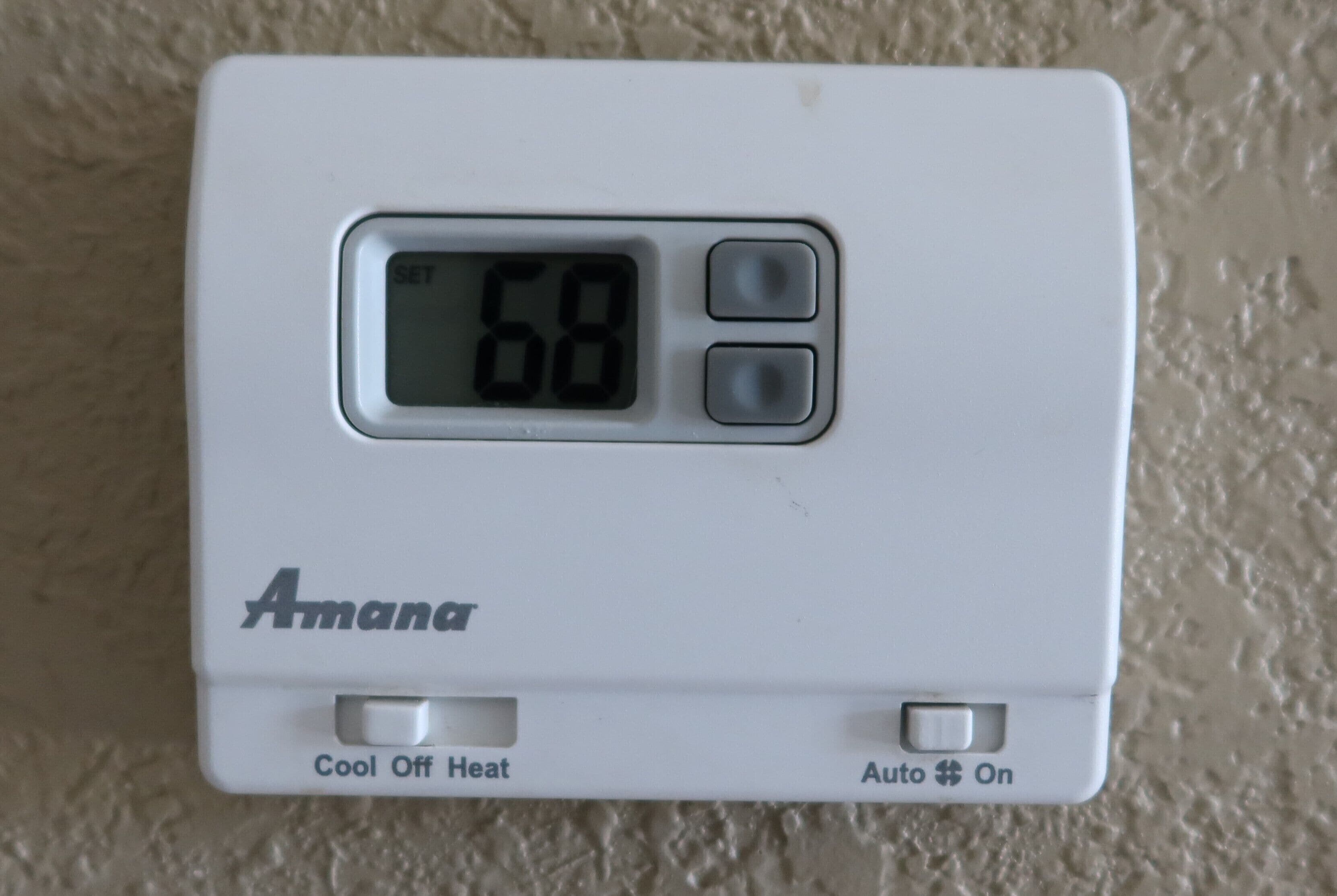 A thermostat with a digital display showing 68 degrees, labeled 'Aman' with 'Cool Off Heat' and 'Auto On' buttons.