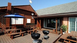 Una terraza de madera con mesas de picnic y dos parrillas.