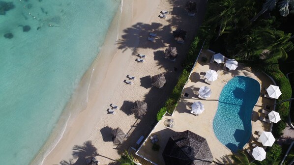 An aerial view of a beach with a swimming pool, sun loungers, and umbrellas. - The Cove Suites at Blue Waters Resort and Spa (St. John's)