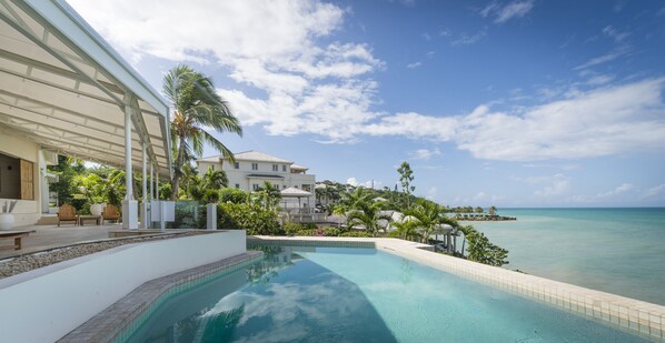 A resort with a pool overlooking the ocean, a covered patio, and lush greenery. - The Cove Suites at Blue Waters Resort and Spa (St. John's)