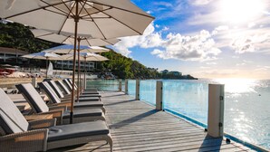 A wooden deck with lounge chairs and umbrellas overlooking a clear blue sea. - The Cove Suites at Blue Waters Resort and Spa (St. John's)