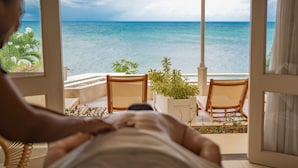 A room with a view of the ocean, a bed, and two chairs. - The Cove Suites at Blue Waters Resort and Spa (St. John's)