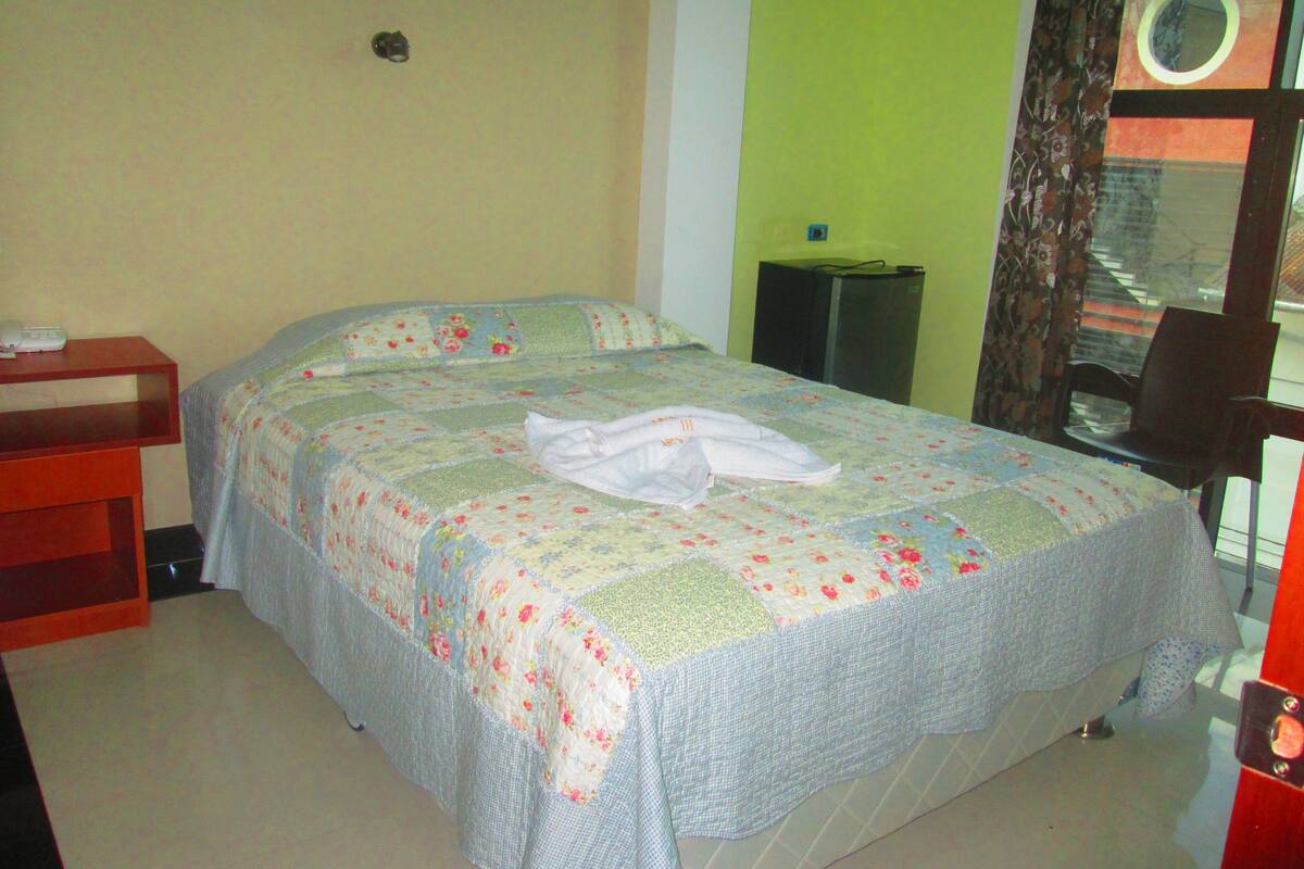 Un dormitorio con una cama, una mesita de noche, una silla y una ventana con cortinas.