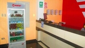 A vending machine with various beverages, a reception desk, and a red wall with a white stripe. - Ari's Hotel III (Iquitos)