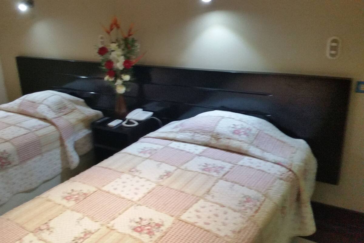 Habitación de hotel con dos camas, una mesita de noche, un teléfono y un arreglo floral.