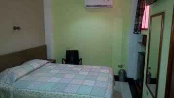 Habitación de hotel con cama, una silla, aire acondicionado, un basurero y un espejo.