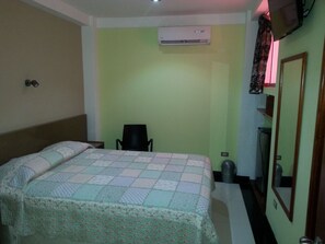 Habitació d'hotel amb un llit, una cadira, un aire condicionat, un cistell de brossa i un mirall.