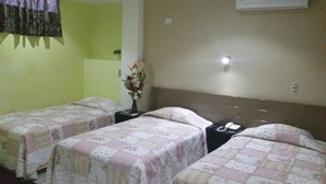 A hotel room with two single beds, a nightstand with a phone, a vase with flowers, and a wall-mounted light. - Ari's Hotel III (Iquitos)