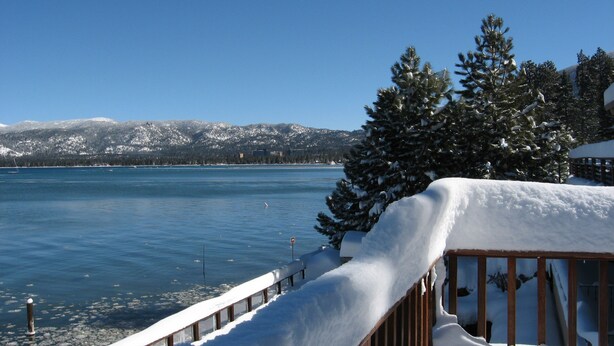 Um deck coberto de neve com vista para um lago e montanhas ao fundo.