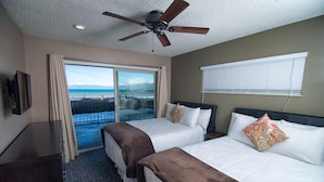 Quarto de hotel com duas camas, ventoinha no teto, televisão e varanda com vista para a praia.
