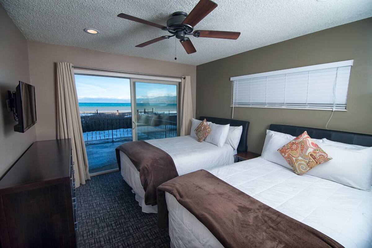 Habitación de hotel con dos camas, ventilador de techo, televisor y balcón con vista a la playa.