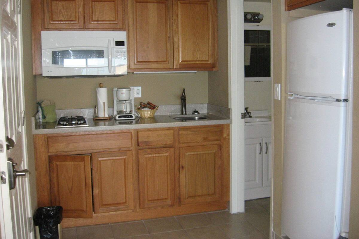 Una cocina con armarios de madera, microondas, cafetera y refrigerador.