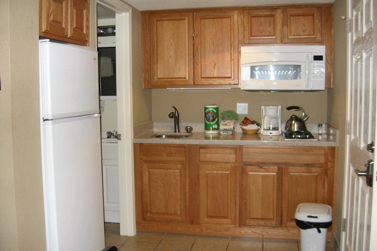 Una cocina con armarios de madera, un refrigerador blanco, un microondas, un fregadero y un cubo de basura.