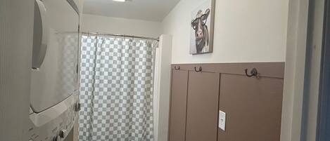 A compact bathroom with a toilet, a checkered shower curtain, a green mat, and a wall-mounted towel rack.