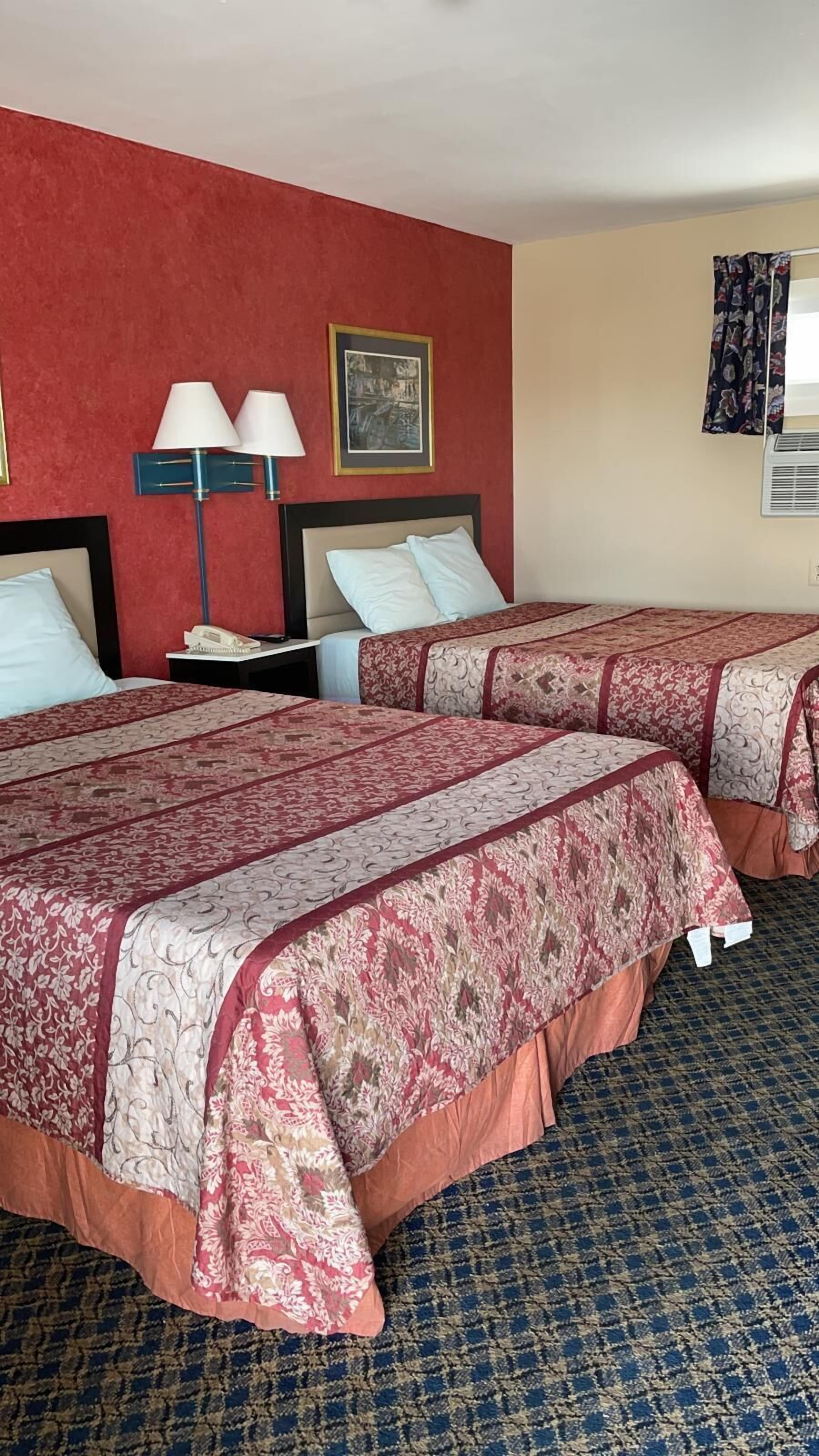 Quarto de hotel com duas camas, uma mesa de cabeceira, uma luminária e um quadro na parede.