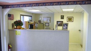 A reception area with a desk, American flag, and various framed pictures on the wall. - Appalachian Motel (Vernon)