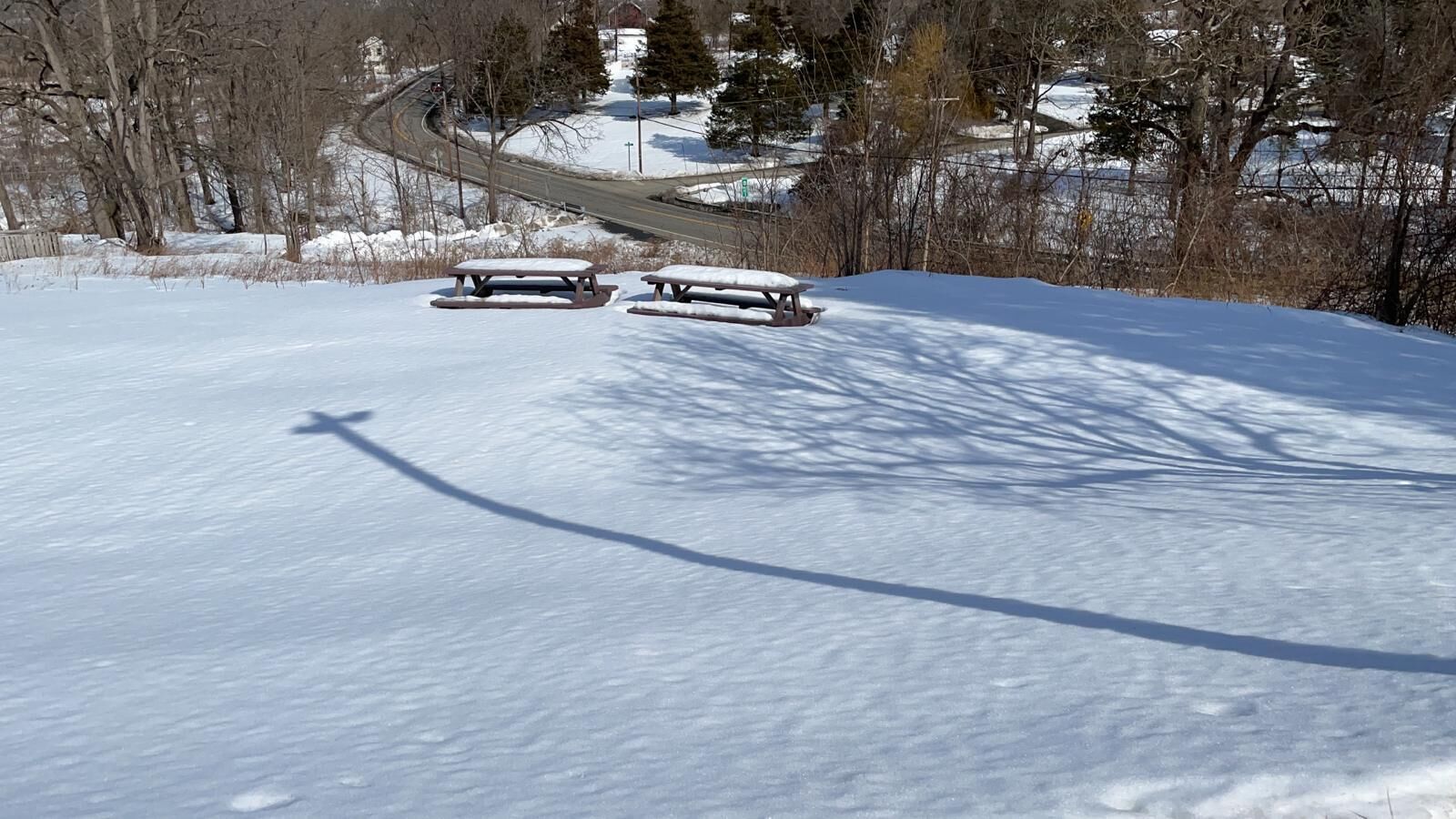 A snow-covered landscape with picnic tables and a road in the background.