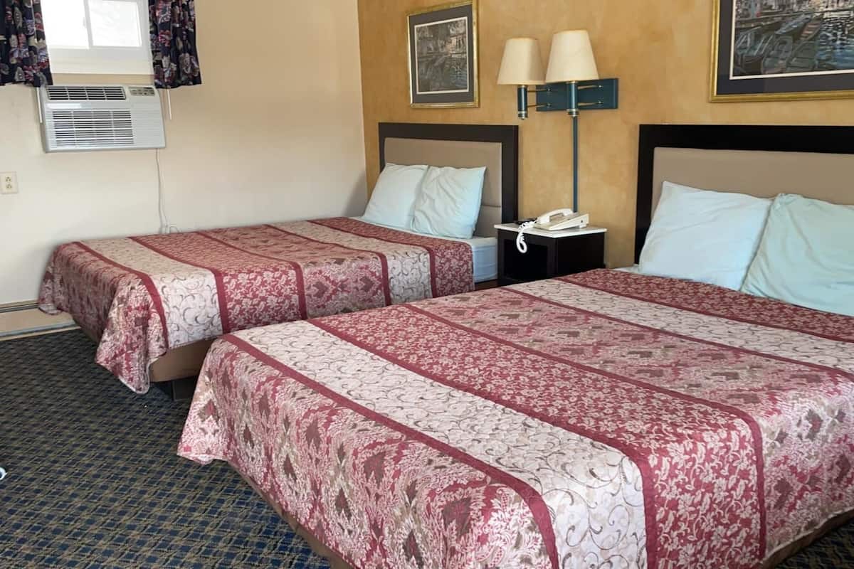 Habitación de hotel con dos camas, cada una con una colcha estampada, una mesita de noche con lámpara y aire acondicionado instalado en la pared.
