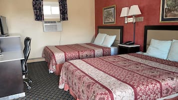 A hotel room with two beds, a desk, a chair, an air conditioning unit, and a nightstand with a lamp.