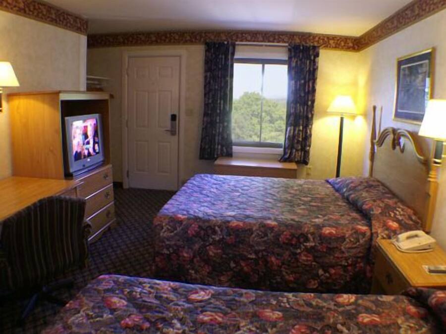 Una habitación de hotel con cama, televisión, escritorio, cómoda y ventana con cortinas.