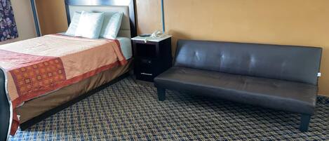 Una habitación de hotel con cama, sofá, mesita de noche y alfombra estampada.