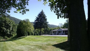 A grassy area with a building in the background, surrounded by trees and a hill. - Appalachian Motel (Vernon)