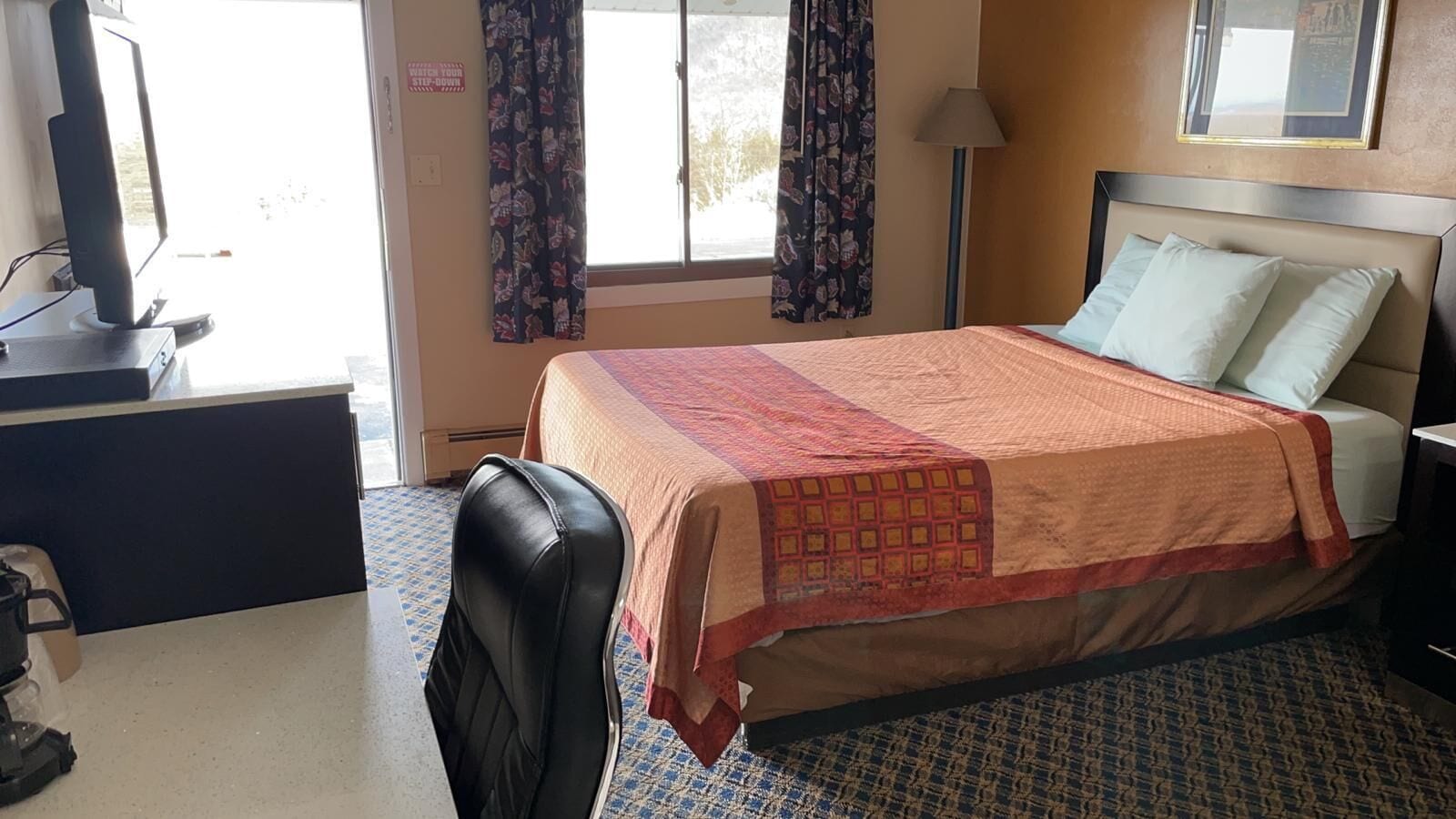 Une chambre d’hôtel avec un lit, un bureau, une chaise, une télévision et une fenêtre avec des rideaux.