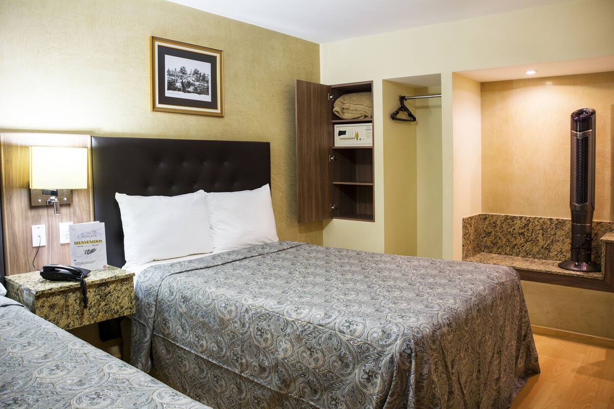 A hotel room with a bed, bedside table, lamp, framed picture, and a wardrobe.