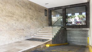 A modern hotel lobby with marble walls, a glass staircase, and a view of the street outside. - Hotel Castropol (Mexico City)