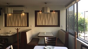 A dining area with a table set for two, a bench, and a window with a view of the street. - Hotel Castropol (Mexico City)