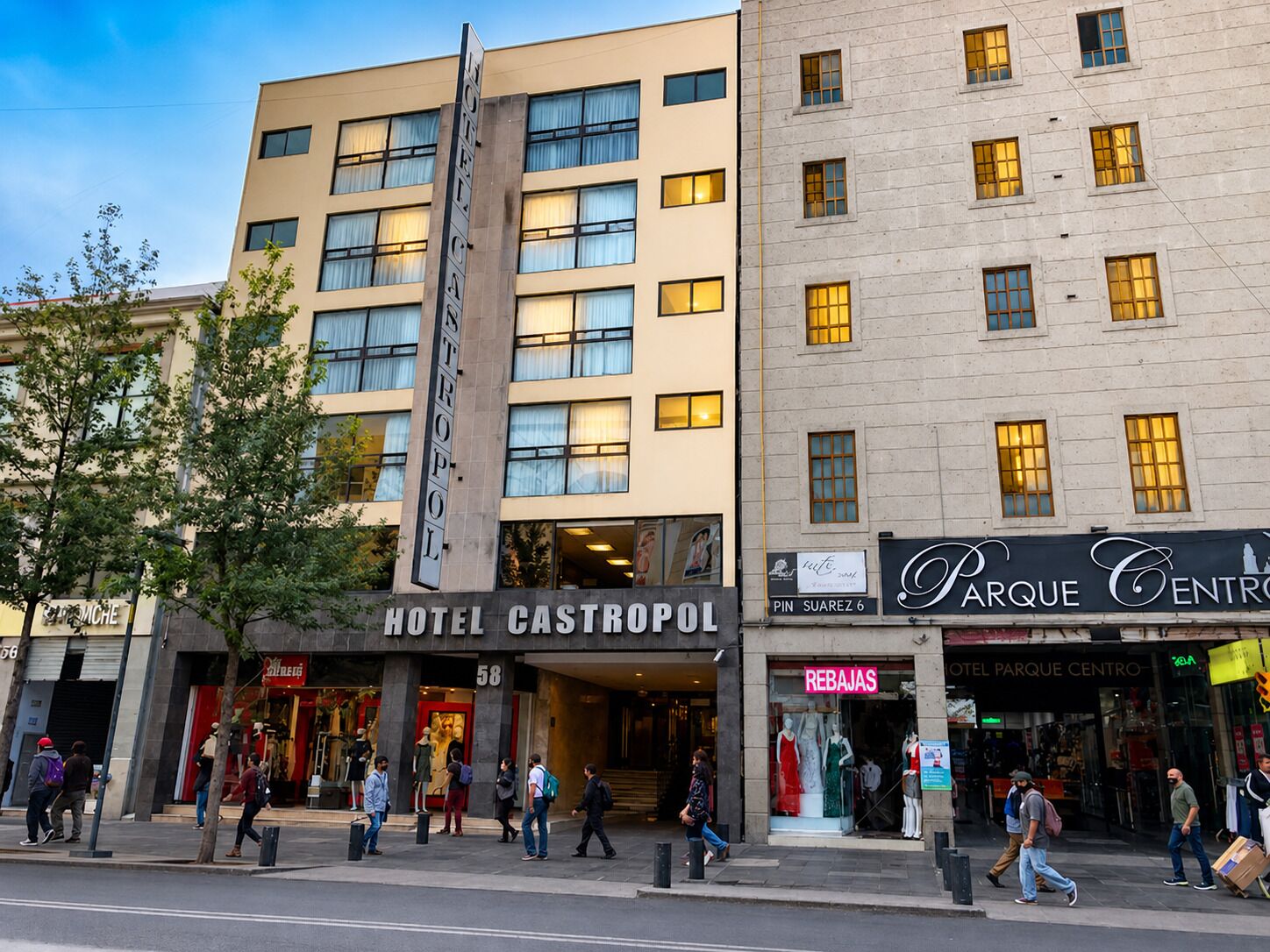 Un hotel con un letrero vertical llamativo, una tienda con maniquíes y una calle peatonal.
